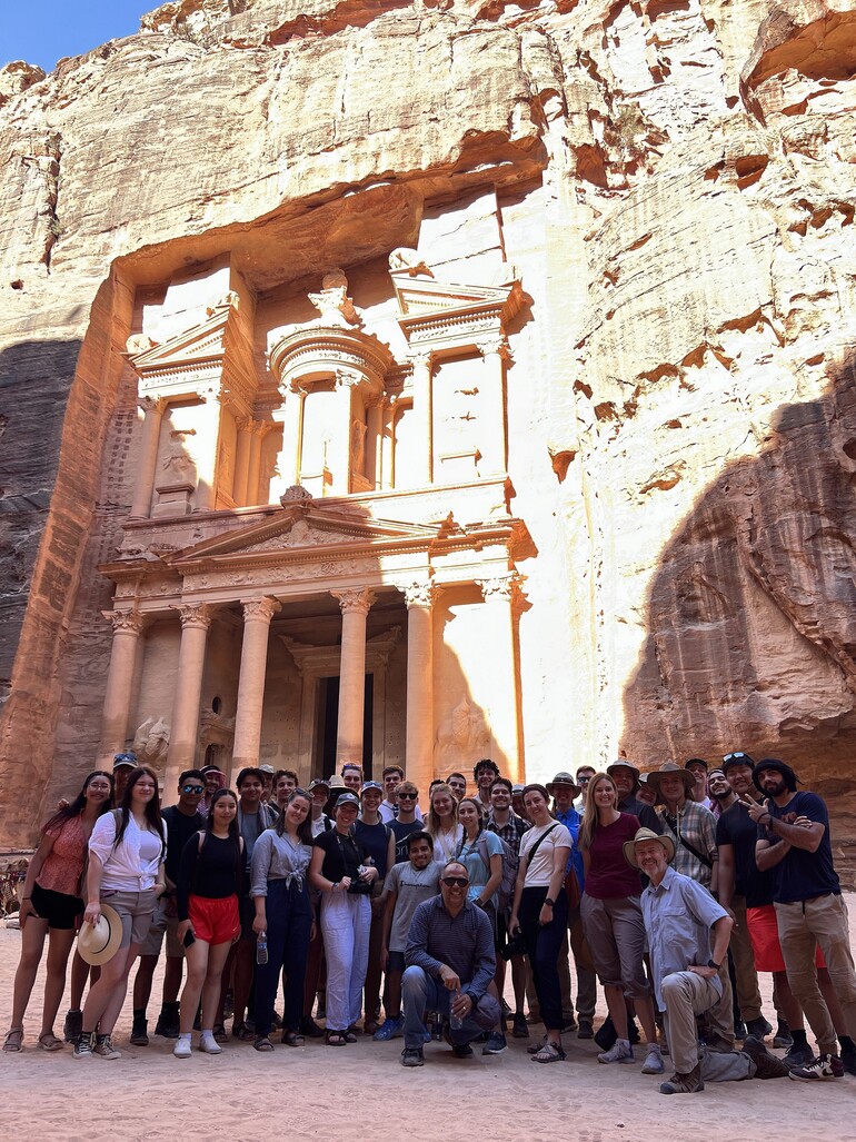 Group of students and professors in front of Petra facade carved in red rock.