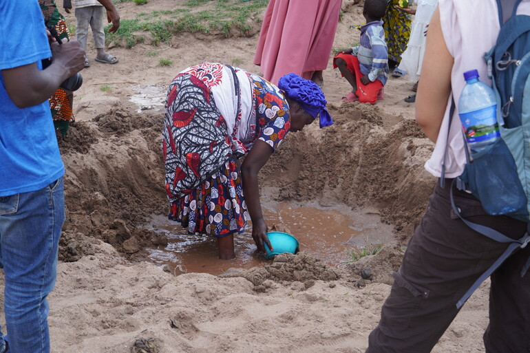 Woman scoops water from muddy puddle