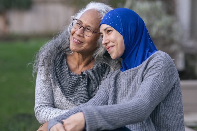 A beautiful Muslim adult female in her 30's is wearing a hijab and spending time with an older non-Muslim woman.