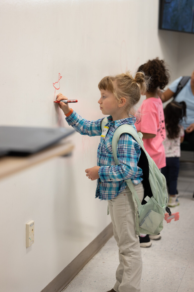 Kids draw on a dry erase wall.